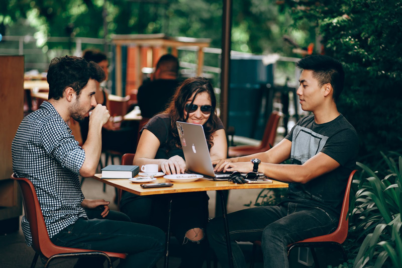 Three members of a startup having coffee and looking at a laptop computer